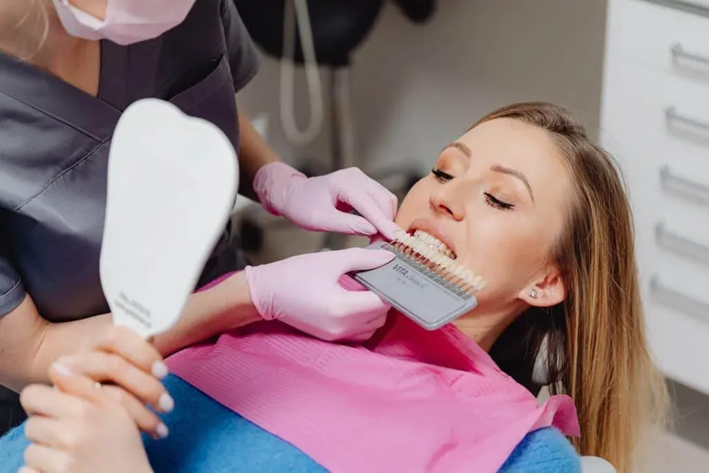 A patient looking in the mirror during a veneer consult exampling different color options