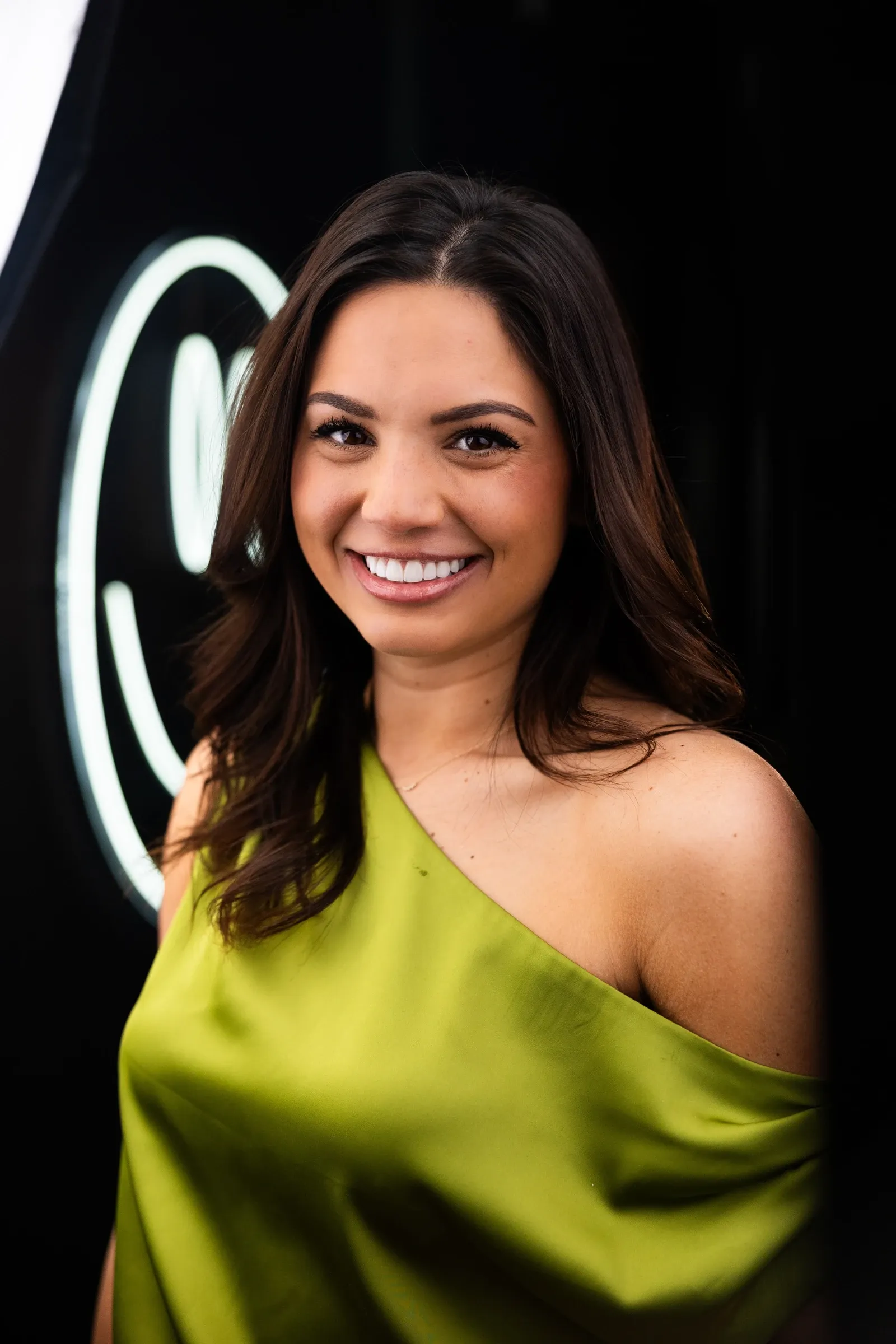 Smiling woman in a green dress photographed at the Vivid Smiles Dentistry neon smile wall in Parker, CO