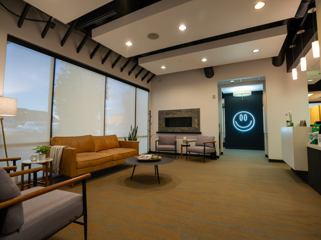 Diagonal Image Of The Waiting Room Of Vivid Smile Dentistry's Parker Colorodo Office. Showing A Couch And A Custom Made Logo Against The Wall