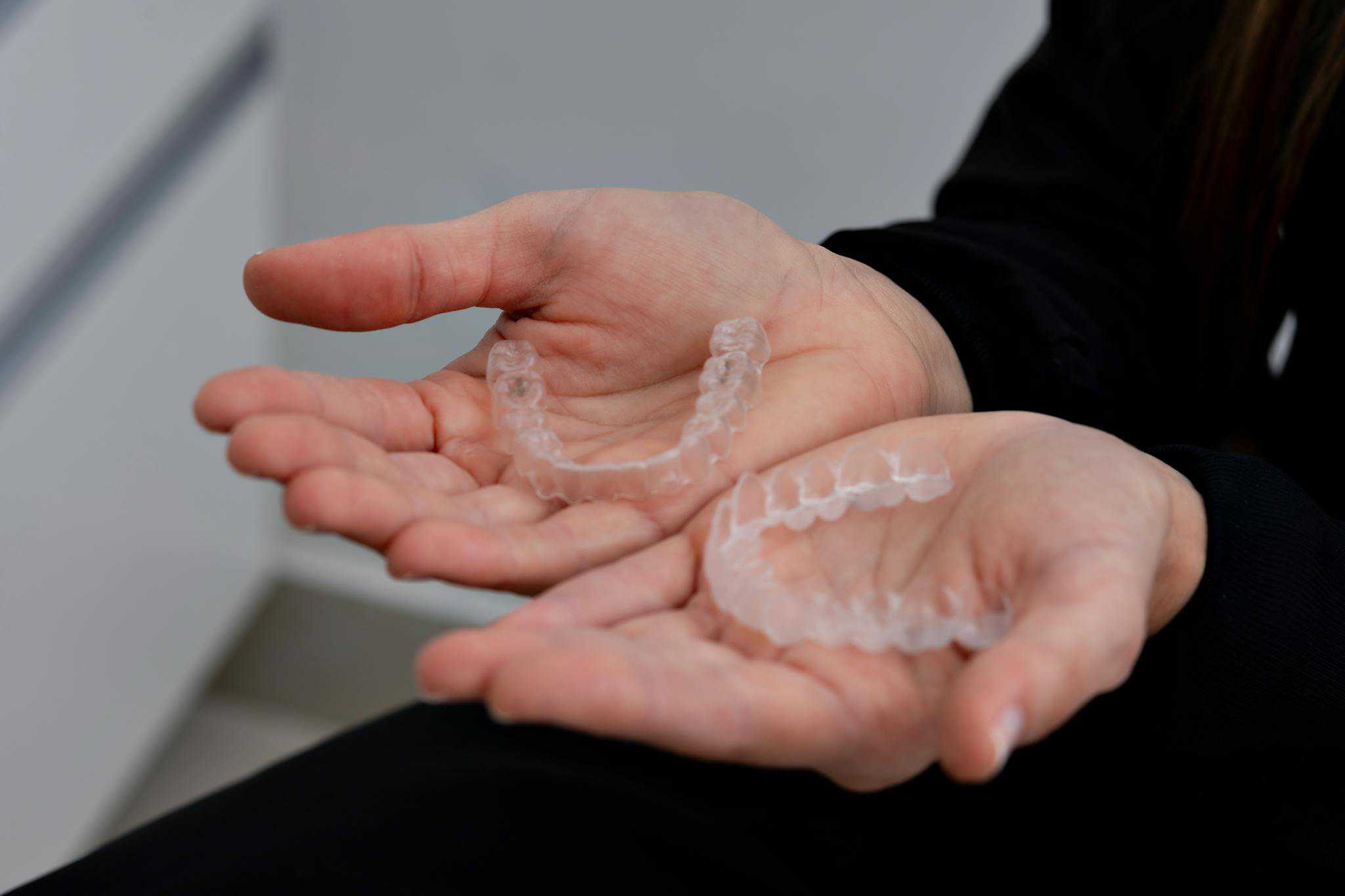 2 hands holding an upper and lower Invisalign clear aligner tray